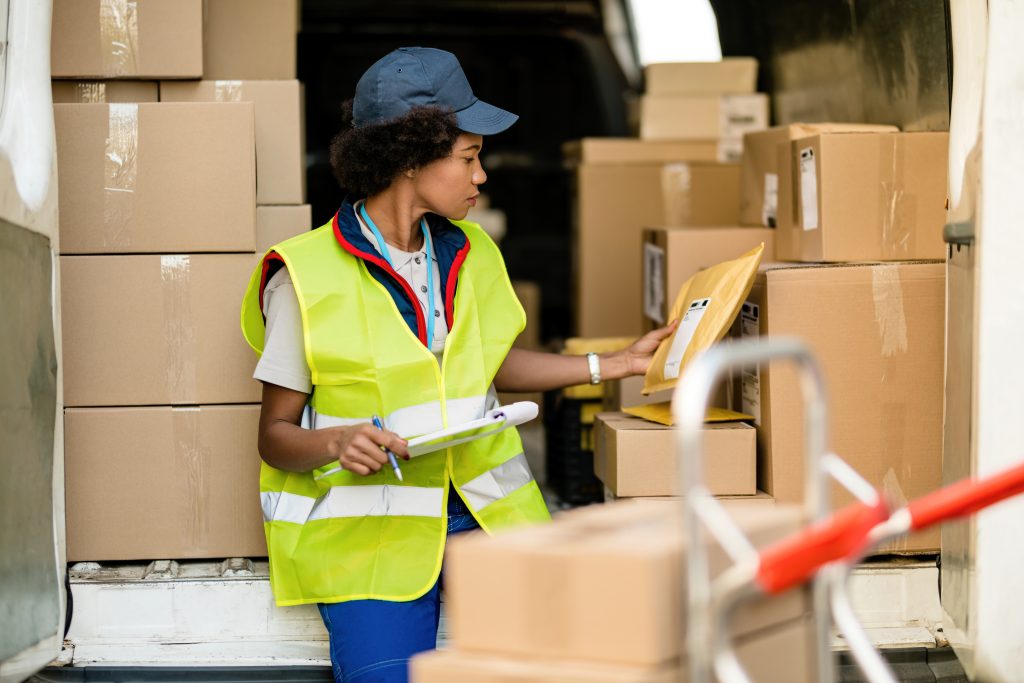 Black female courier working and checking packages in a delivery van.